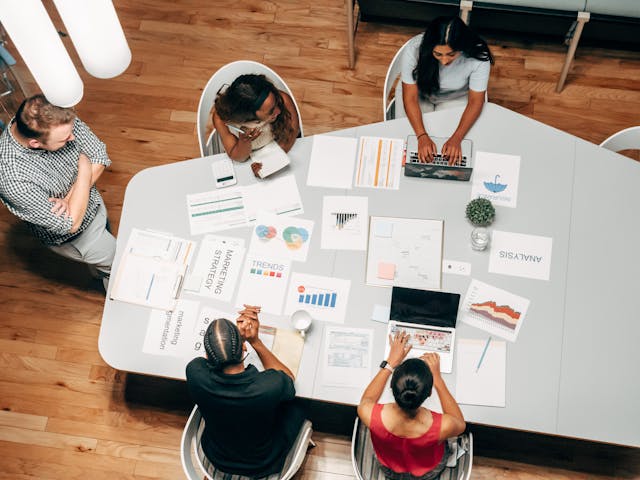 A diverse group of individuals gathered around a table, engrossed in their work with papers, discussing CRM for drip campaigns