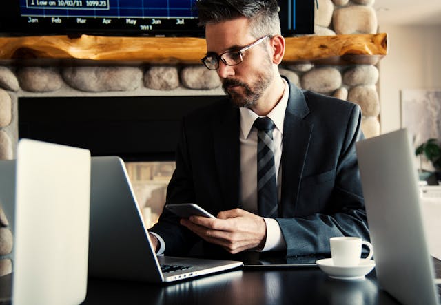 A lawyer in a suit and tie sitting at a desk with a laptop and cell phone, using digital tools